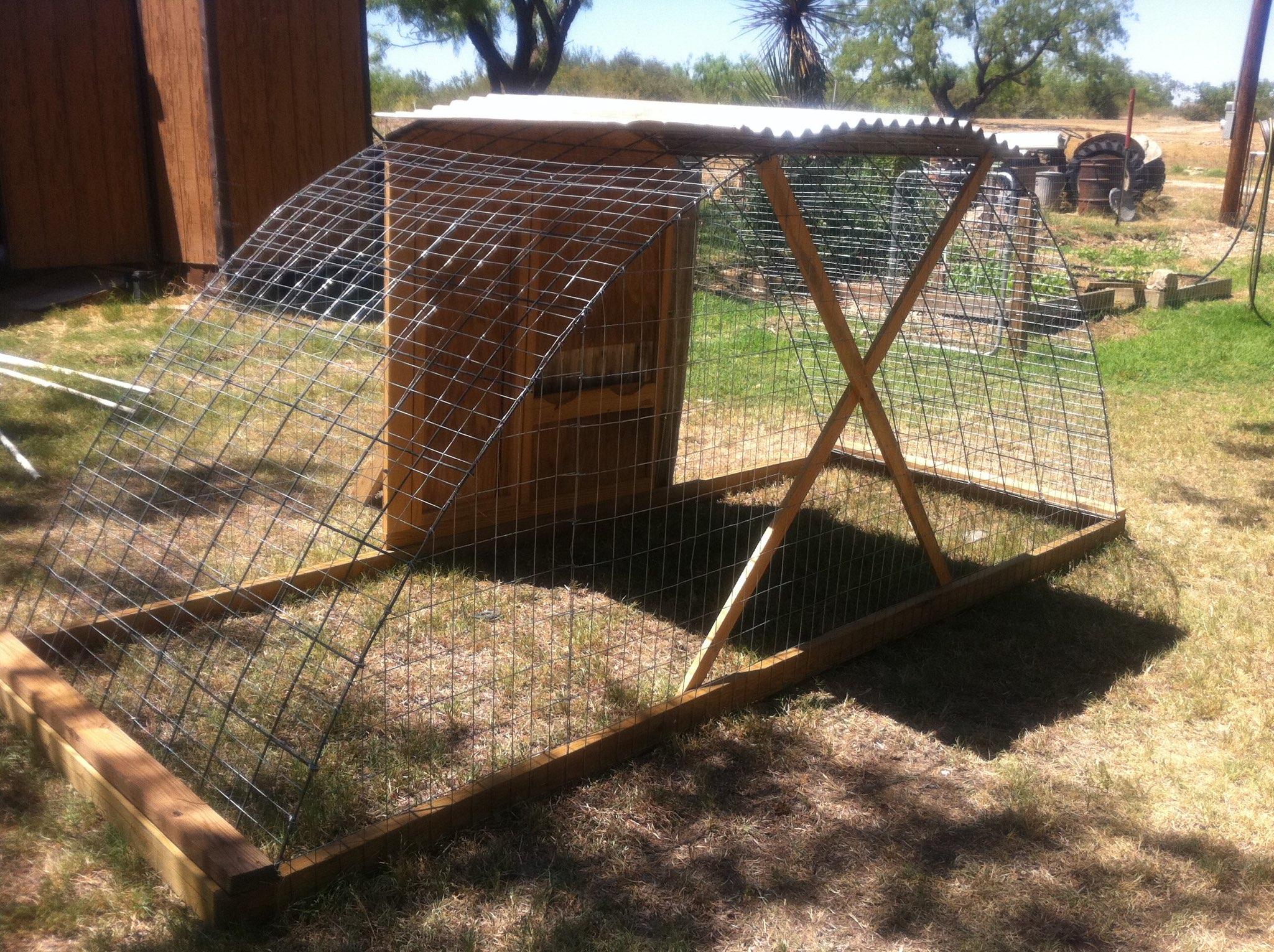 A hoop-style chicken tractor made from a curved cattle panel with hardware cloth sides, sitting in a backyard with hens foraging inside
