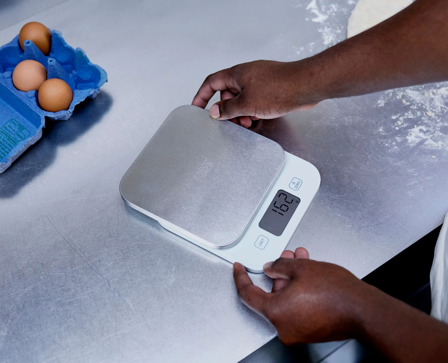 A small digital kitchen scale set to grams on a countertop next to a shallow container used for weighing small animals