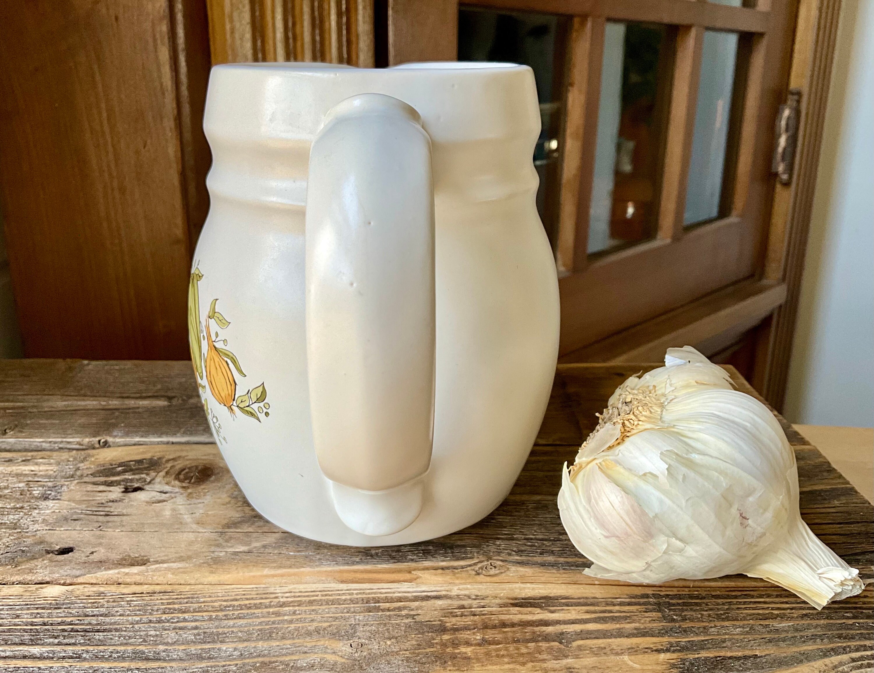 Fresh garlic cloves being lightly crushed on a cutting board next to a pitcher of water, prepared for mixing into a backyard chicken waterer